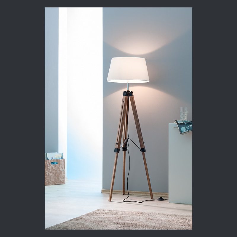 Stehlampe mit weißem Stoffschirm auf Dreibeinstativ aus dunklem Holz